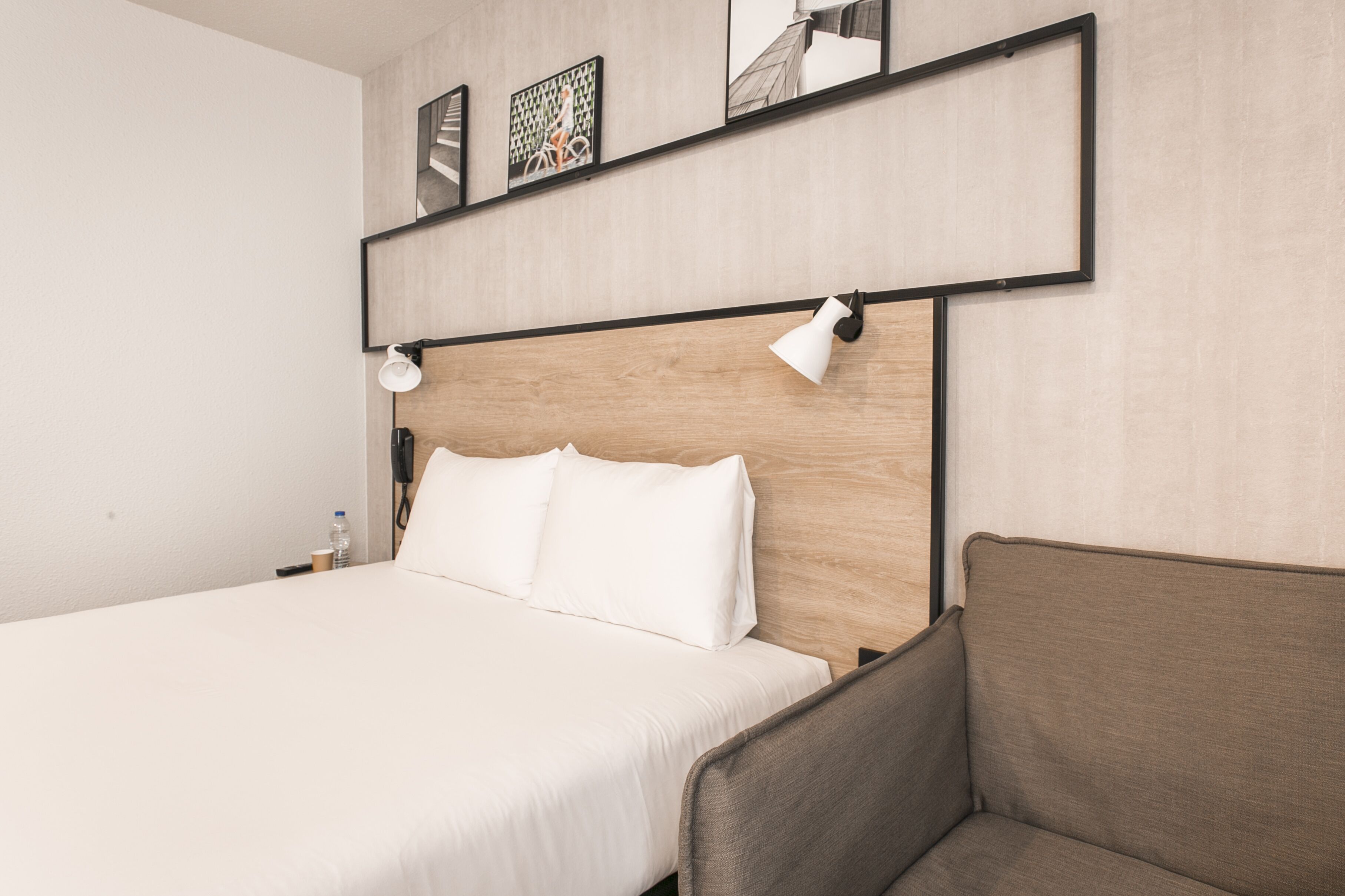 A hotel room with a bed, a nightstand, a lamp, and a wall-mounted shelf with pictures.