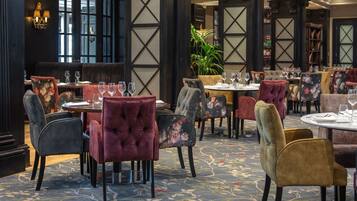 A restaurant with plush seating, tables set with wine glasses, and a patterned carpet.