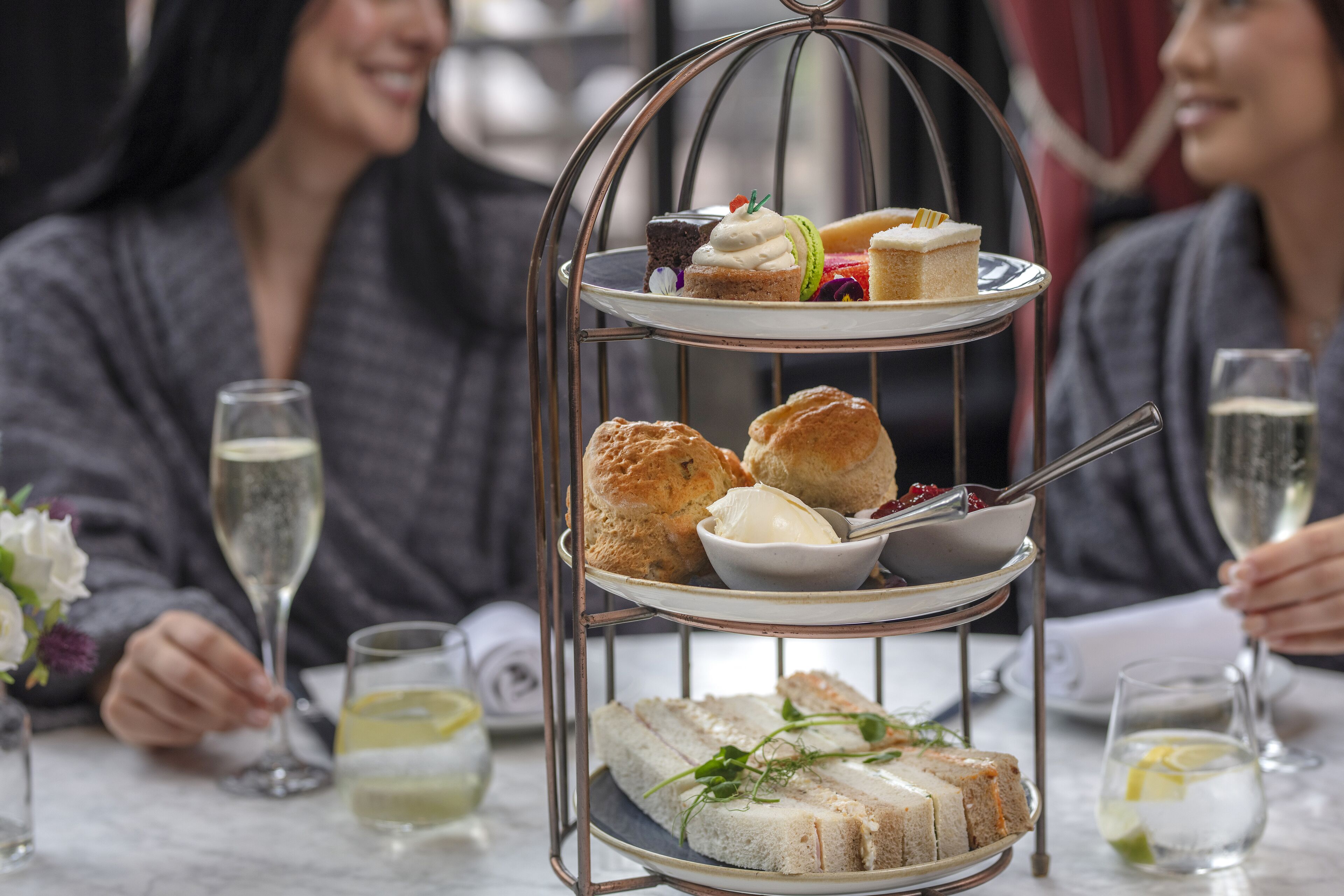 A three-tiered dessert stand with various pastries and sandwiches on a table.