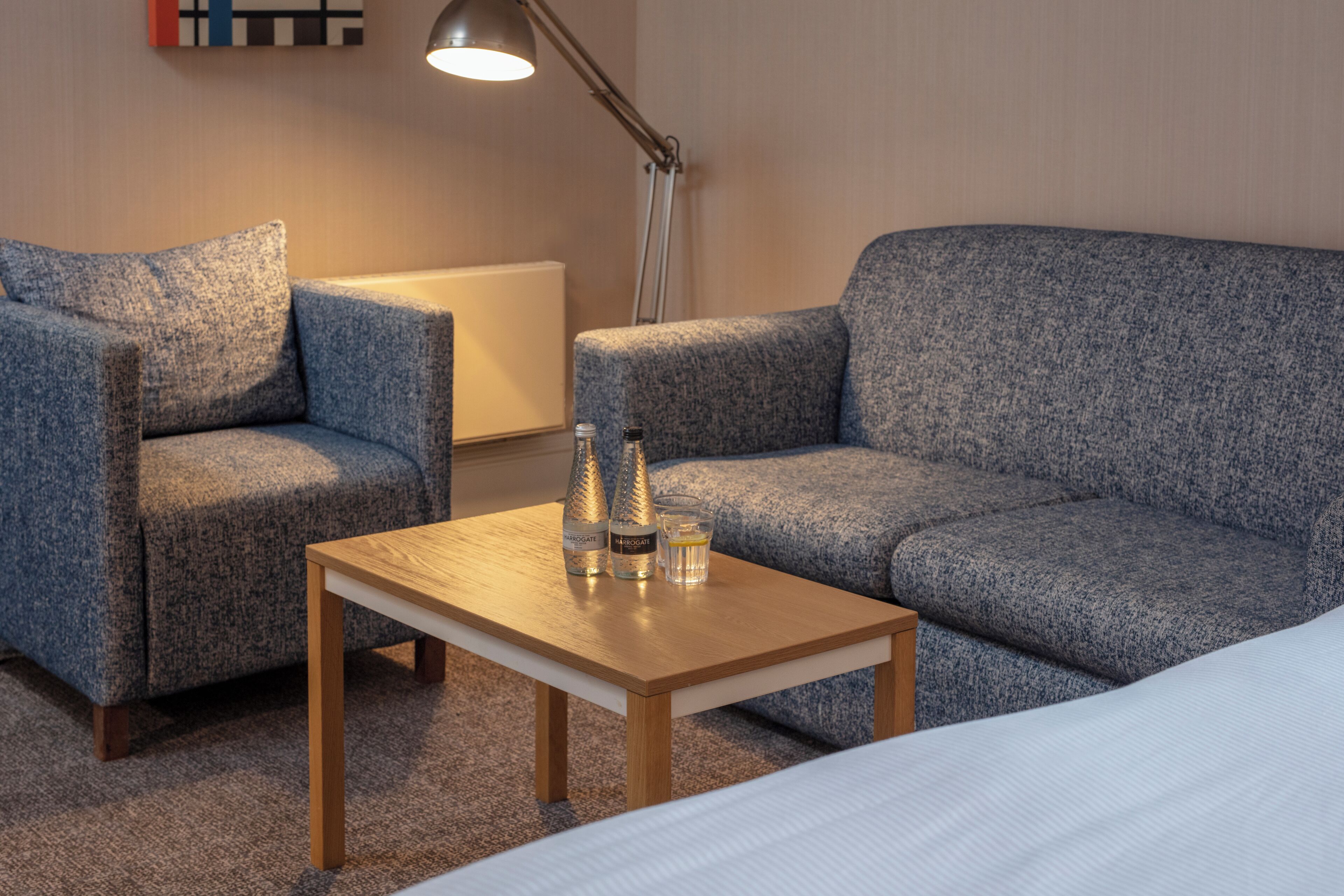 A room with a blue sofa, a wooden table with bottles and a glass, and a lamp.