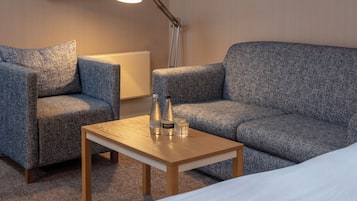 A room with a blue sofa, a wooden table with bottles and a glass, and a lamp.
