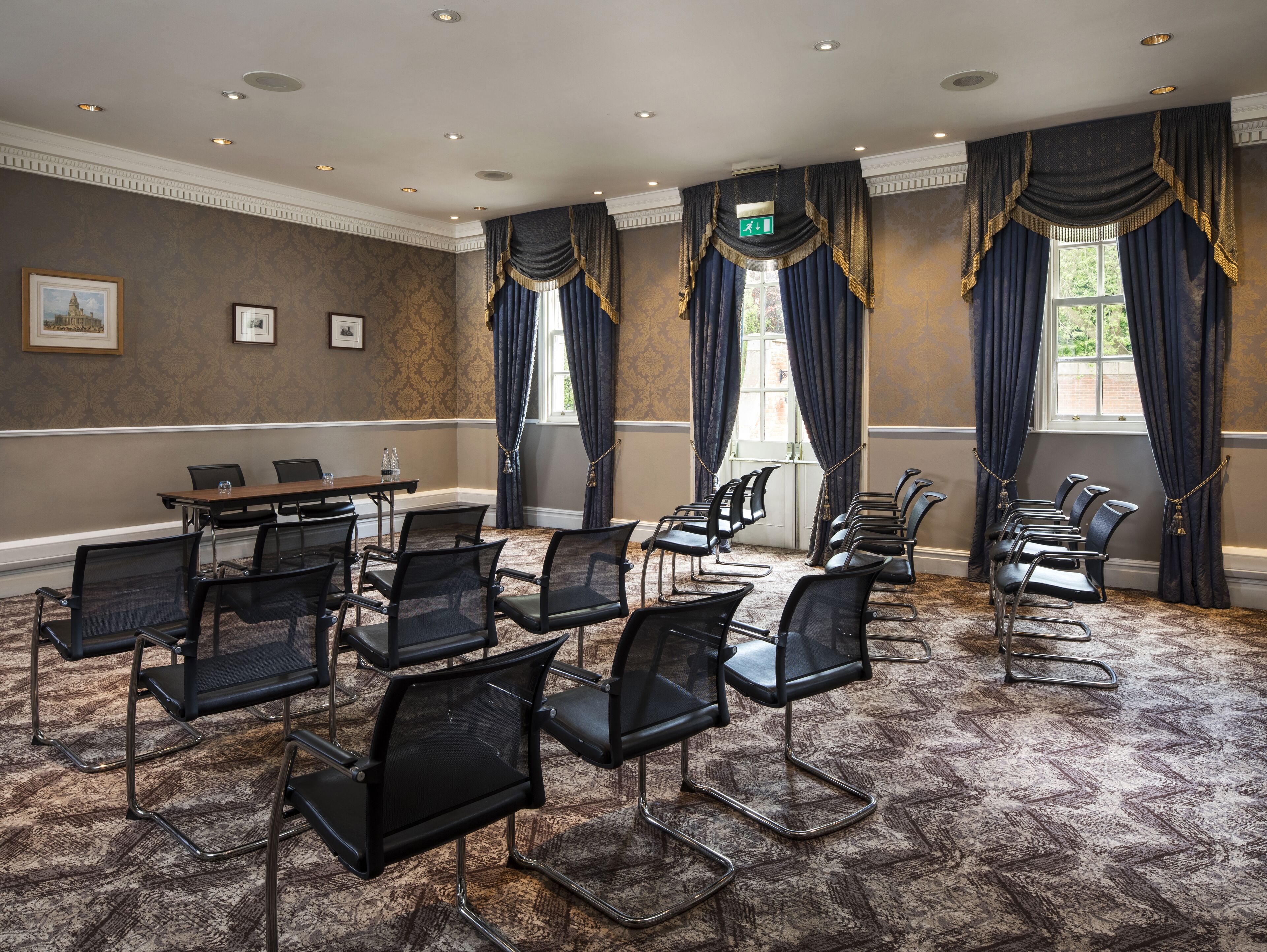A conference room with a long table and multiple chairs, large windows with curtains, and a carpeted floor.