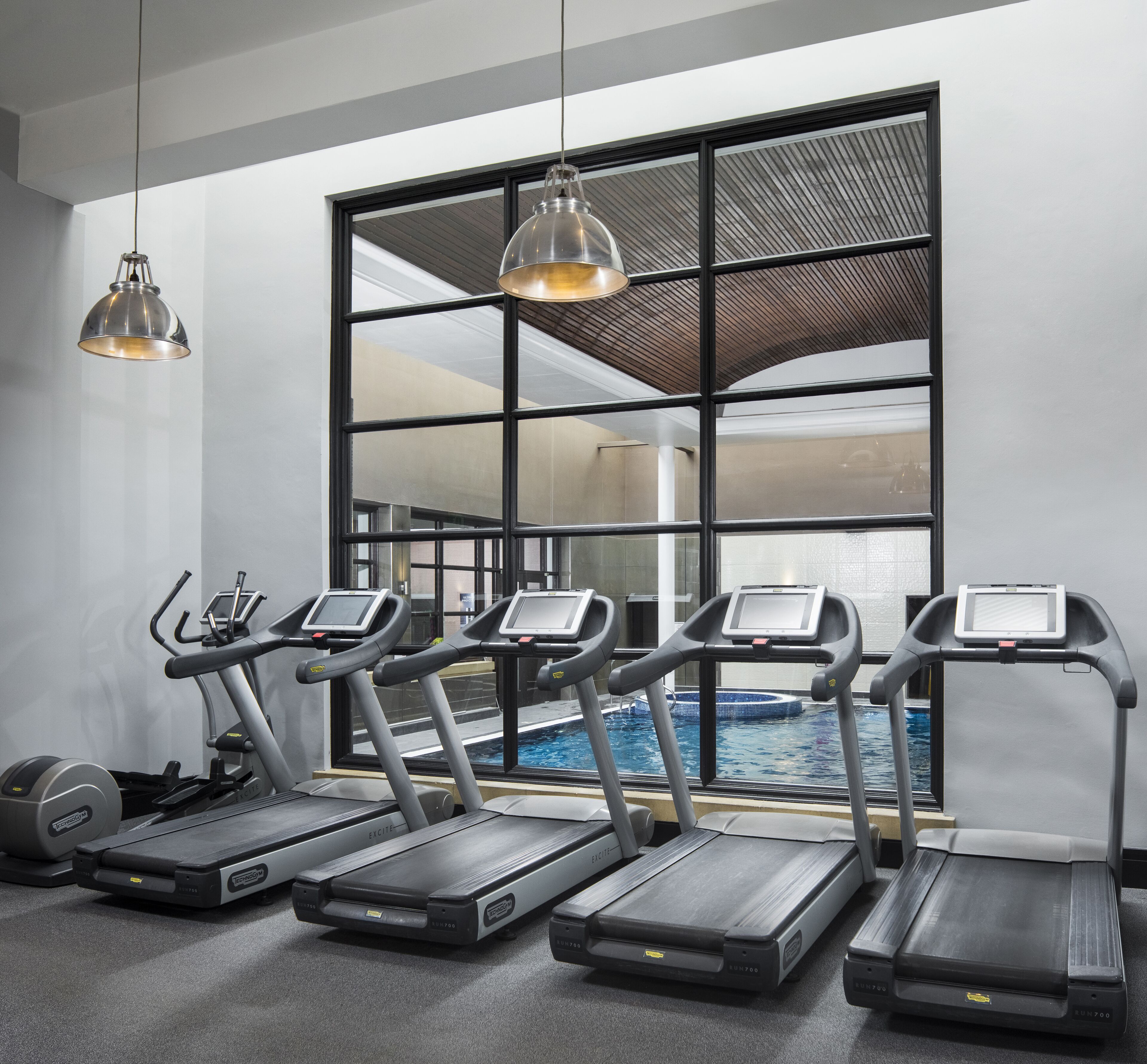 A gym with treadmills, a stationary bike, and a pool visible through large windows.