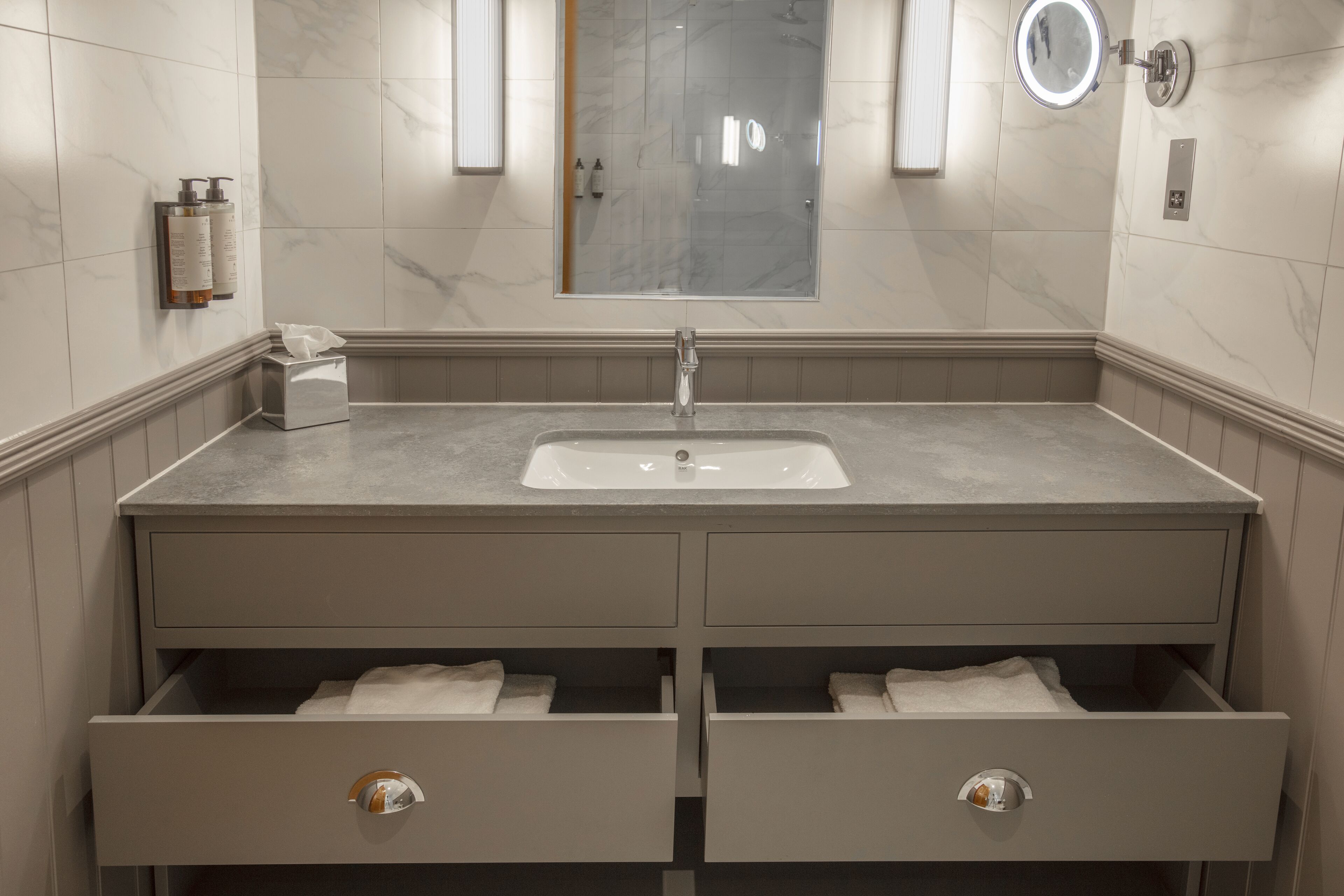 Un baño moderno con pared de azulejos de mármol, un espejo grande, un lavamanos y dos cajones con toallas.