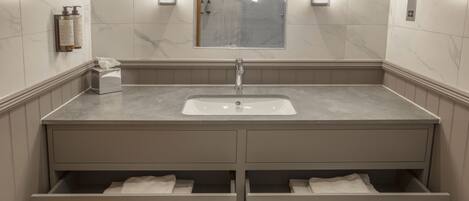 A modern bathroom with a marble-tiled wall, a large mirror, a sink, and two drawers with towels.