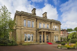 A large, historic stone building with a grand entrance, multiple windows, and a well-maintained garden.