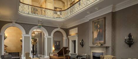A grand lobby with a piano, multiple seating areas, and a high ceiling with a skylight.