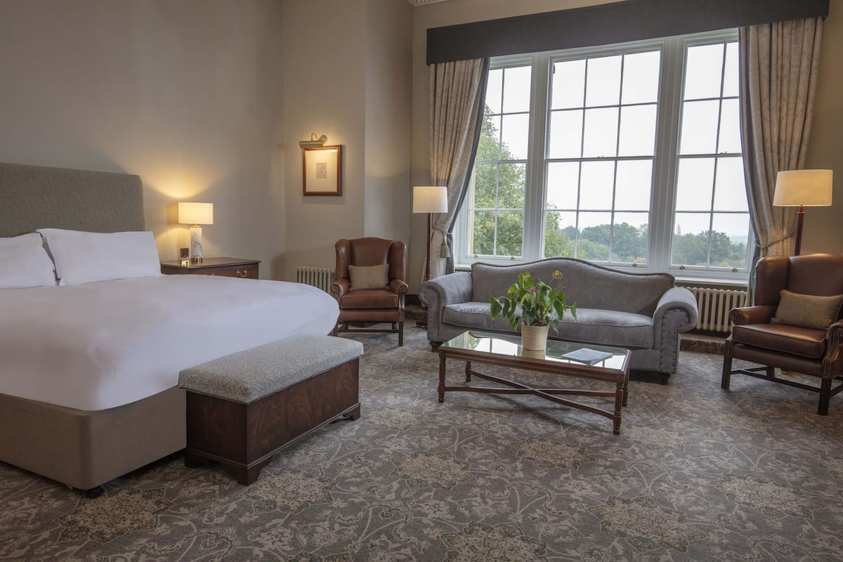 A hotel room with a large bed, two armchairs, a sofa, a coffee table, and a window with curtains.