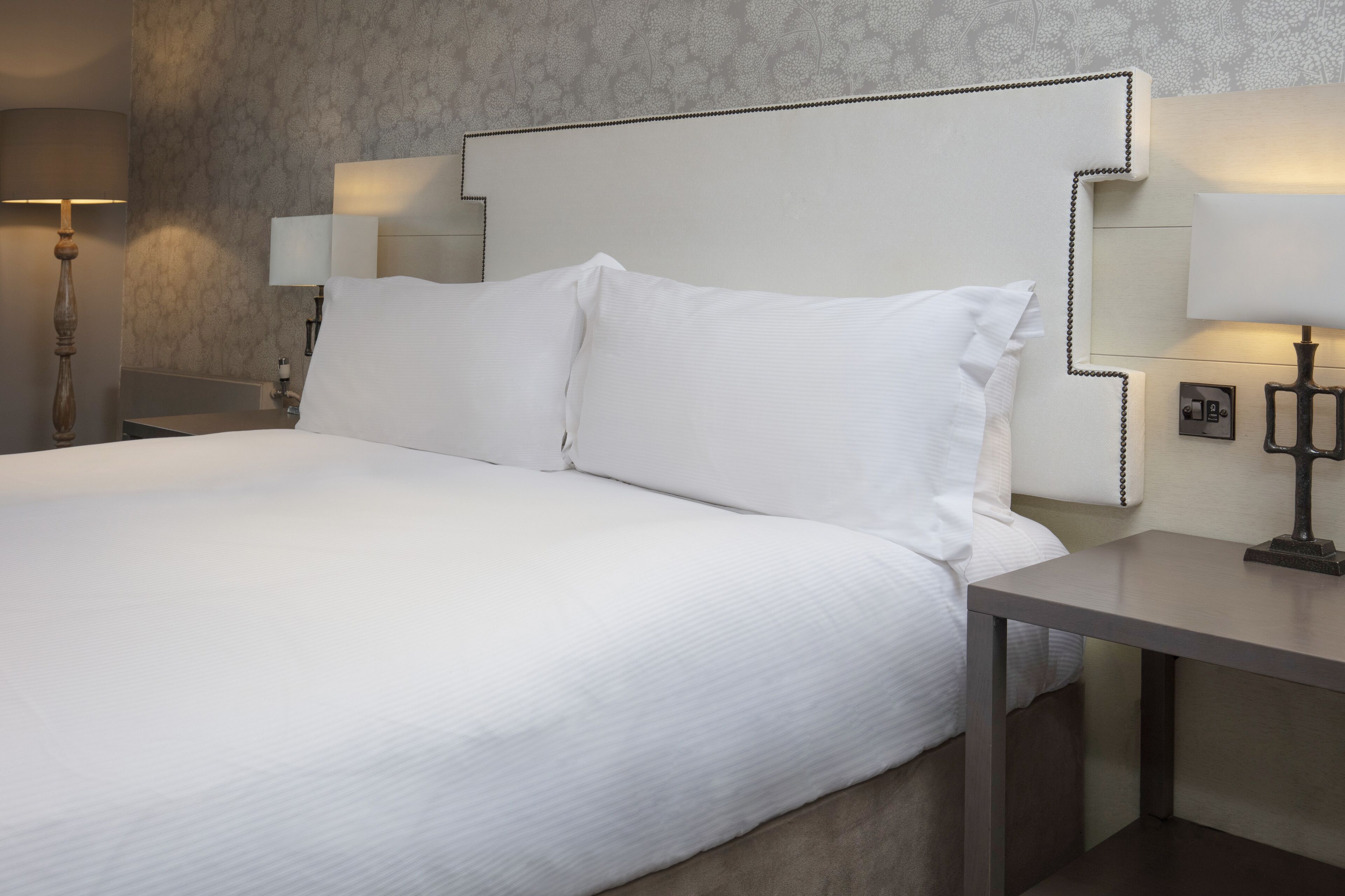 A neatly made bed with white linens, a headboard with a unique design, and bedside lamps.
