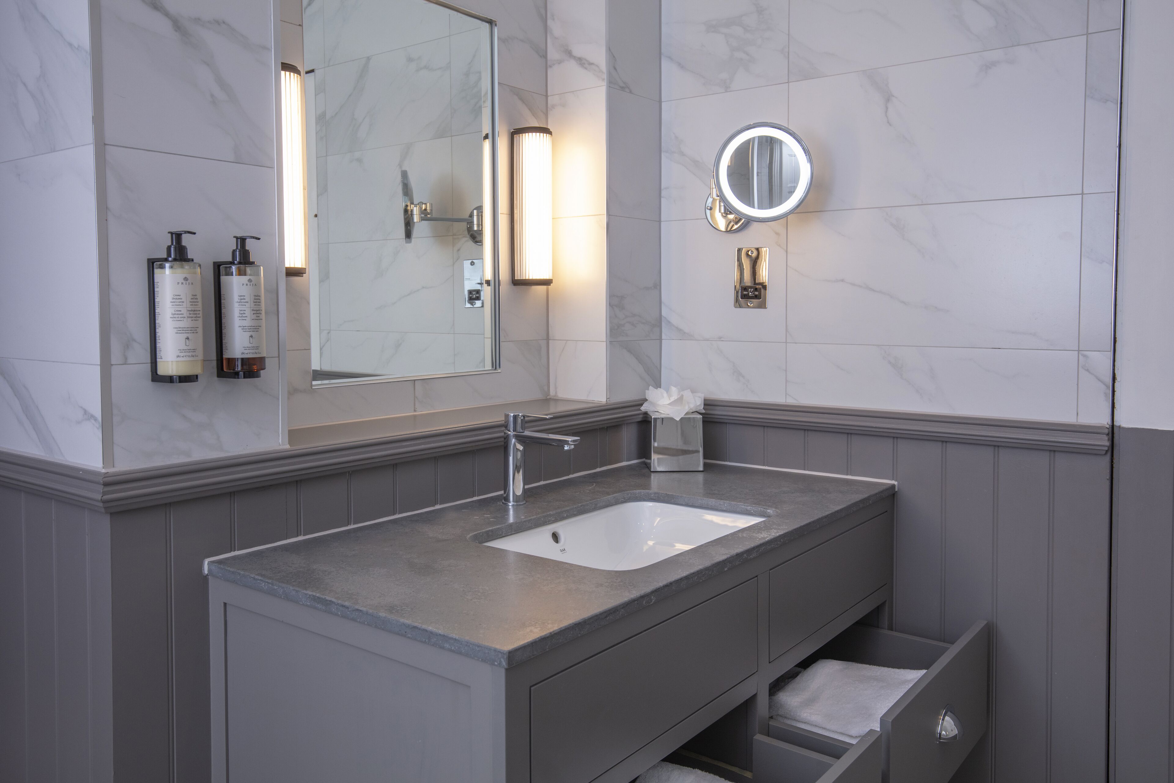 Un baño moderno con pared de mármol, un espejo grande, un lavamanos y dos botellas de champú.