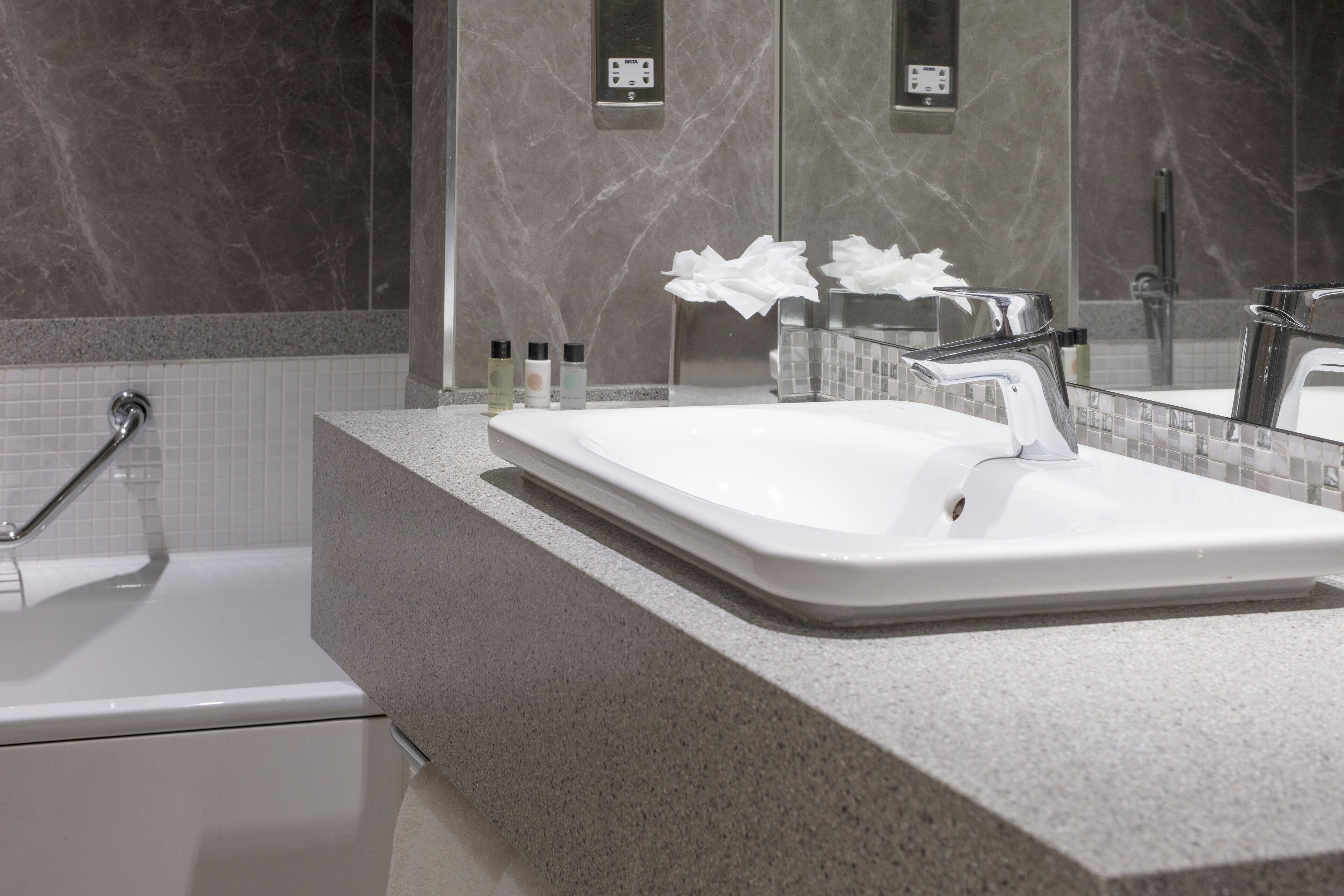 Un baño moderno con un lavabo blanco, paredes de mármol y un espejo grande.