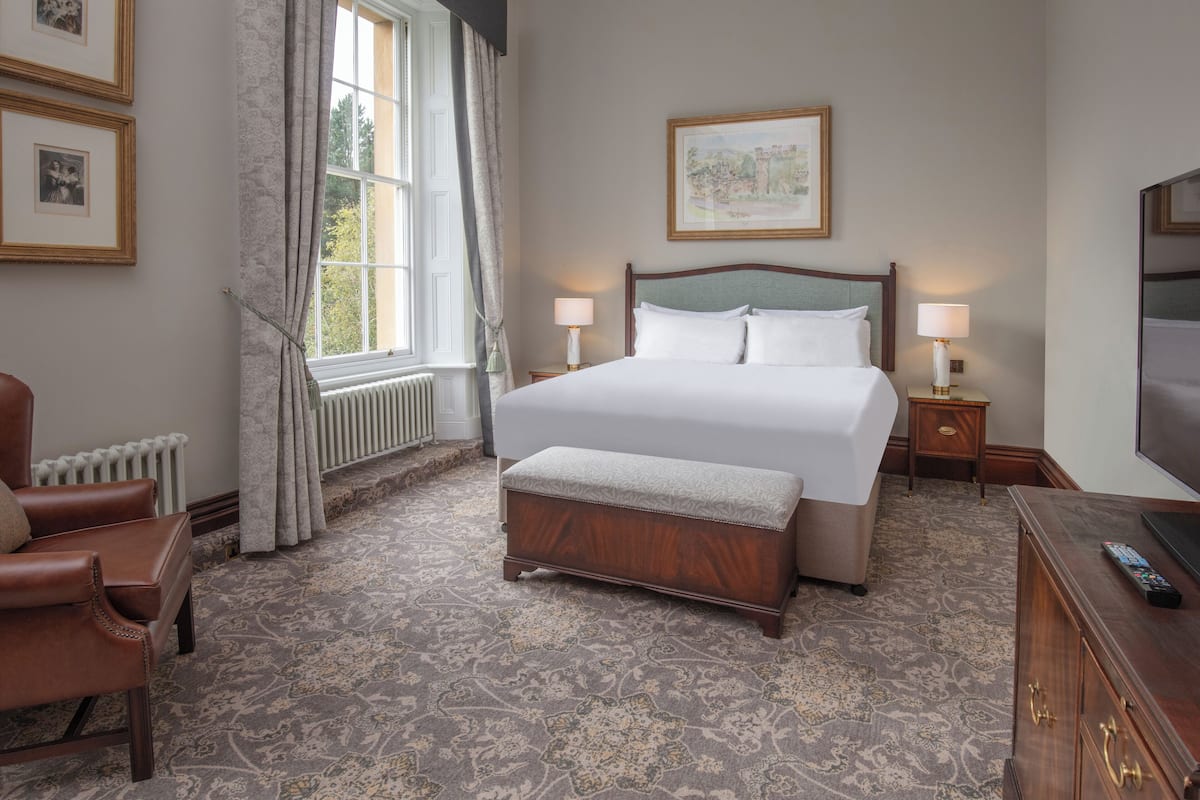 A hotel room with a large bed, two bedside tables with lamps, a wooden bench, a TV, and framed pictures on the wall.