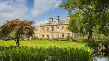 A large, historic building with a well-maintained lawn and a pond in the foreground.