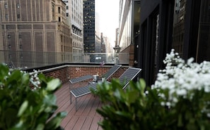 Terraço no telhado com vista para o horizonte da cidade, apresentando uma parede de tijolos e grades de metal.
