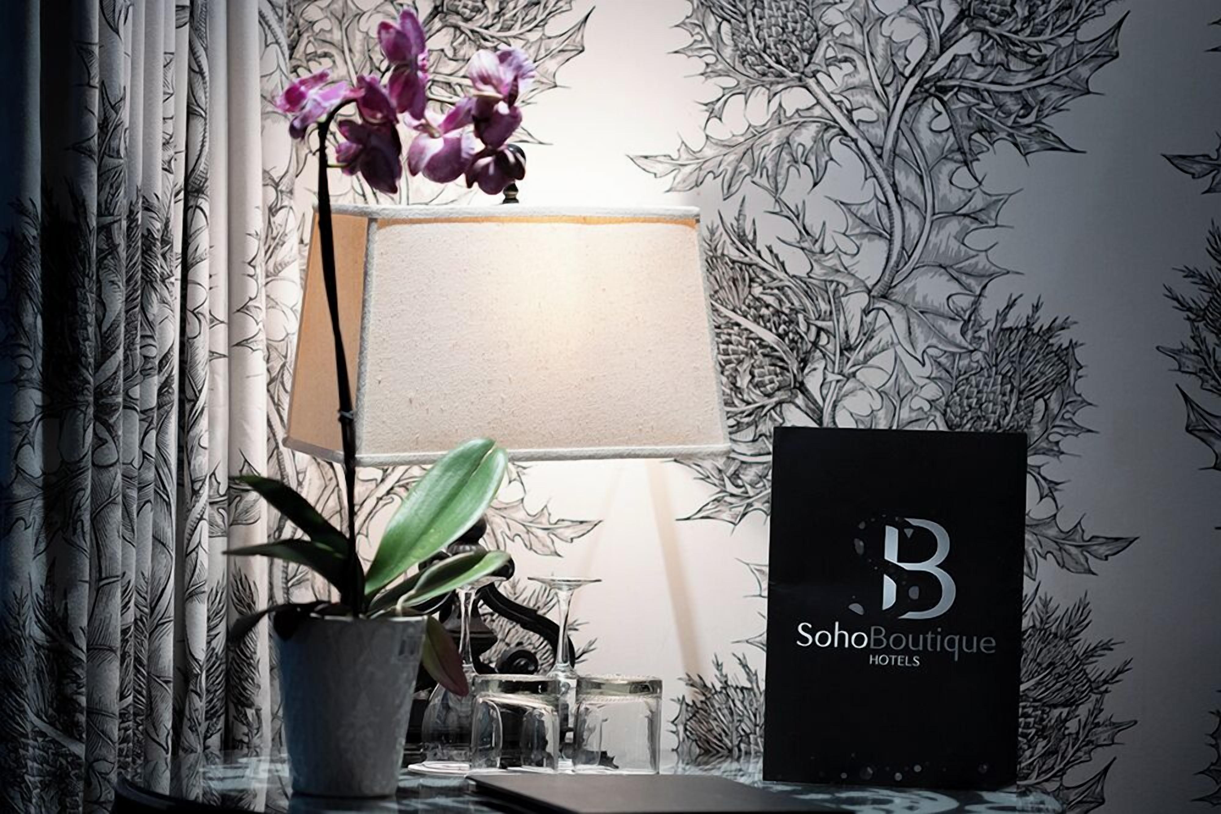 A room with a potted plant, a lamp, and a framed sign for SohoBoutique Hotels.