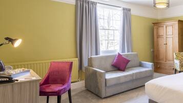 Ein Zimmer mit einem hellgrauen Sofa, einem roten Sessel, einem Holzschrank und einem Bett.