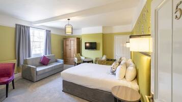 A hotel room with a large bed, a sofa, a chair, a television, and a cabinet.