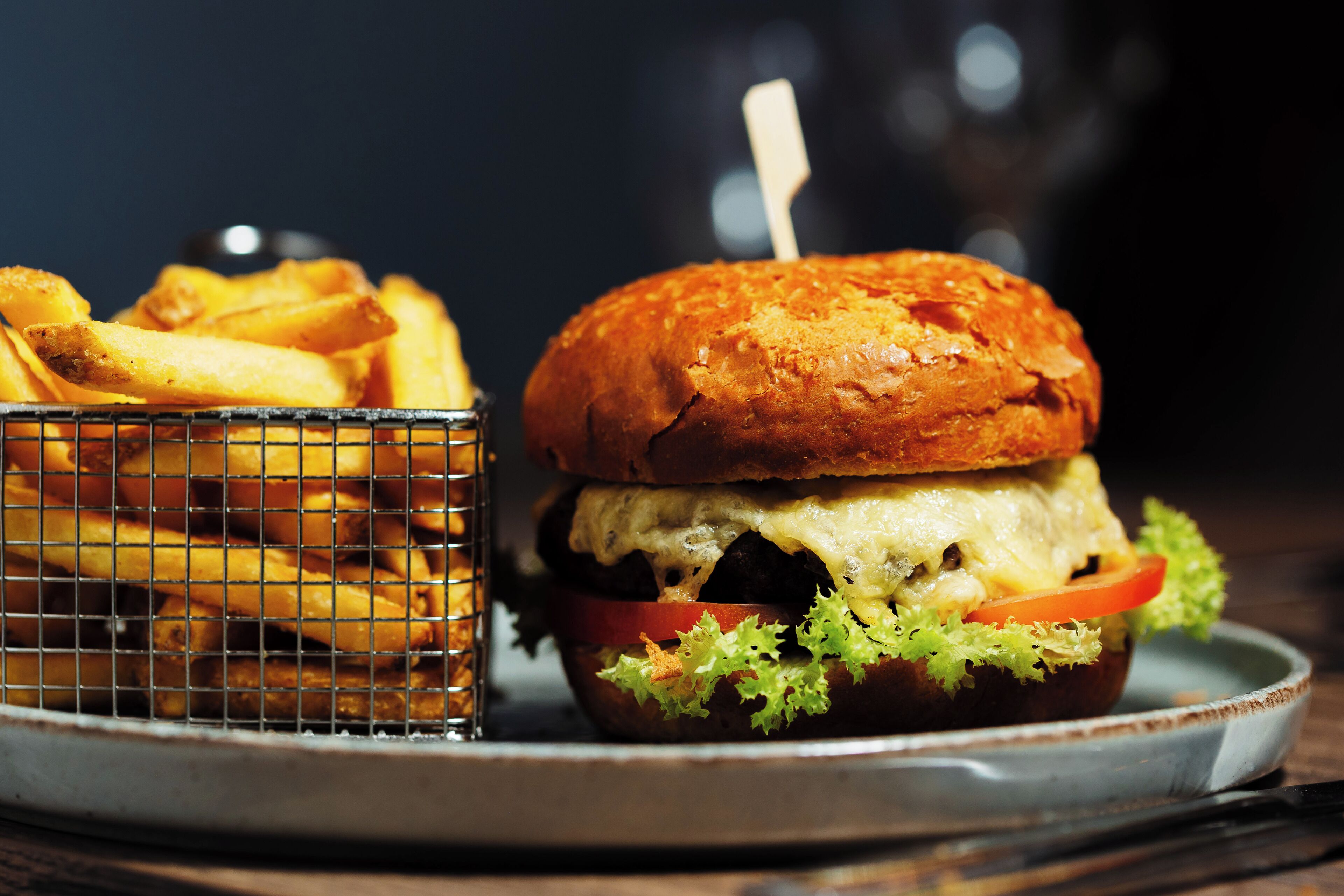 En burger med salat, tomat og ost, samt en kurv pommes frites.
