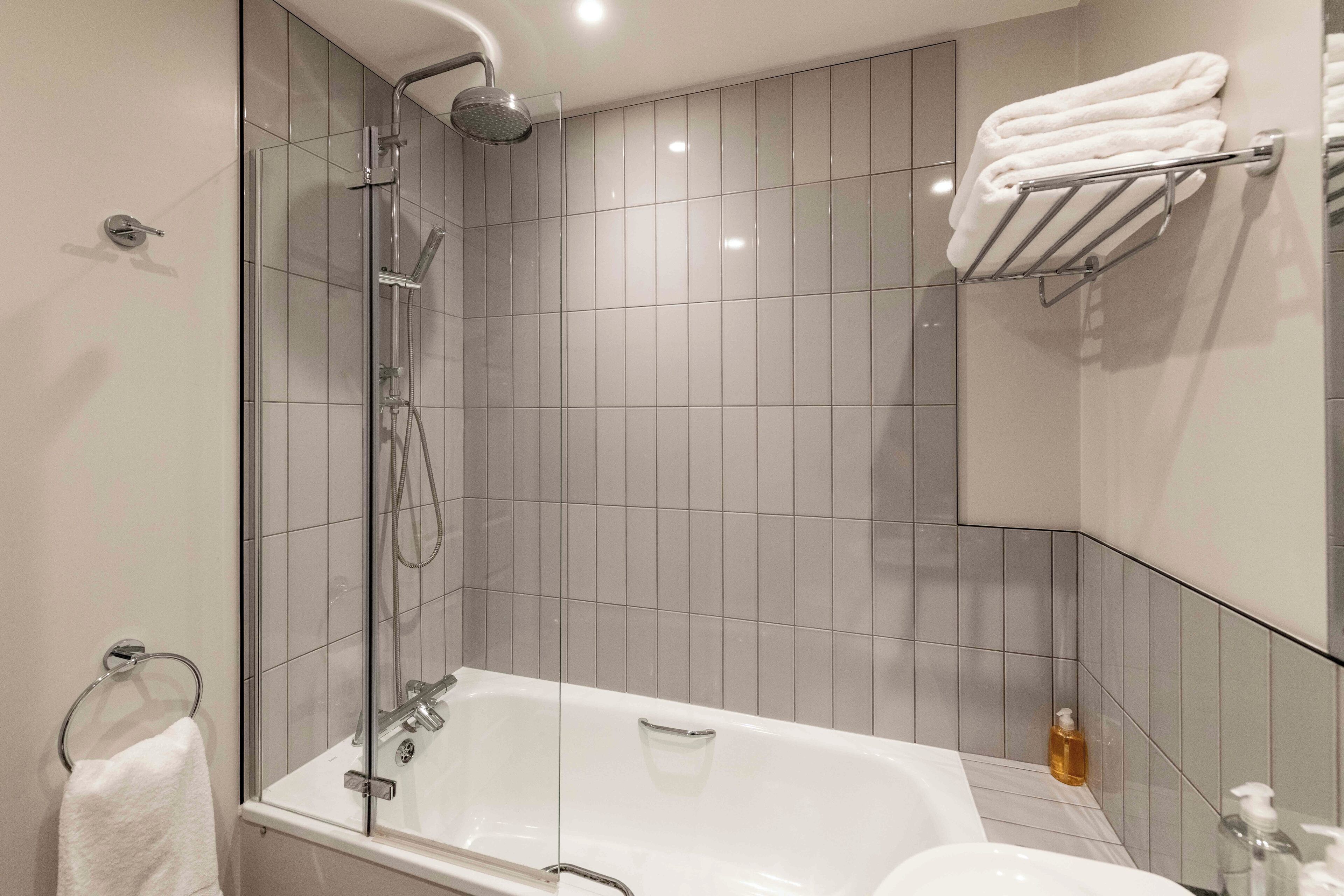 Un baño moderno con ducha de vidrio, bañera blanca y un perchero con toallas dobladas.