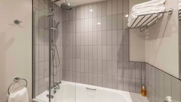 Un baño moderno con ducha de vidrio, bañera blanca y un perchero con toallas dobladas.