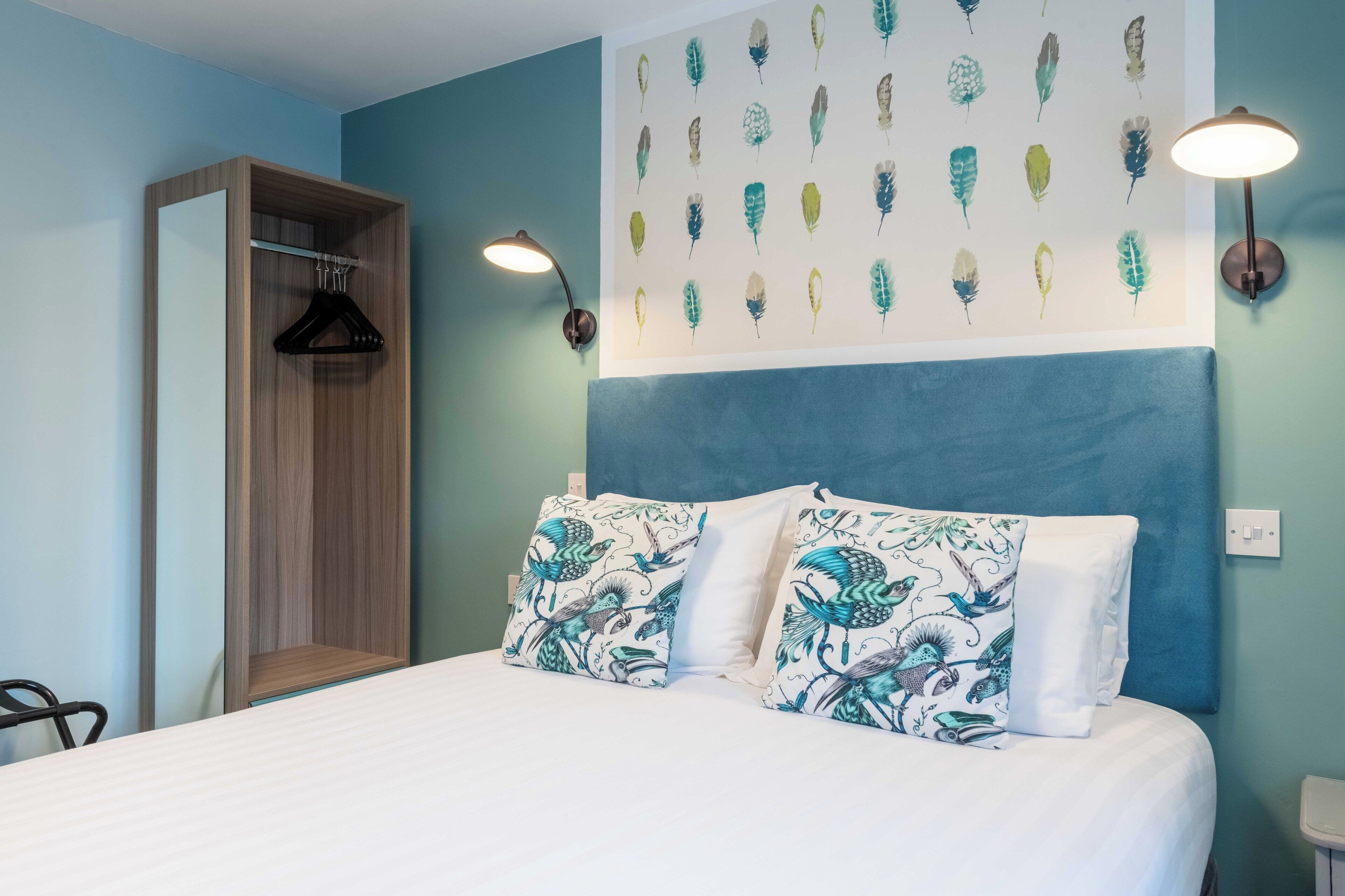 Un dormitorio con cama, armario colgante, una pared decorada con arte de plumas y una lámpara de pared.
