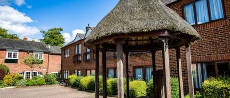A brick building with a thatched gazebo in the courtyard.