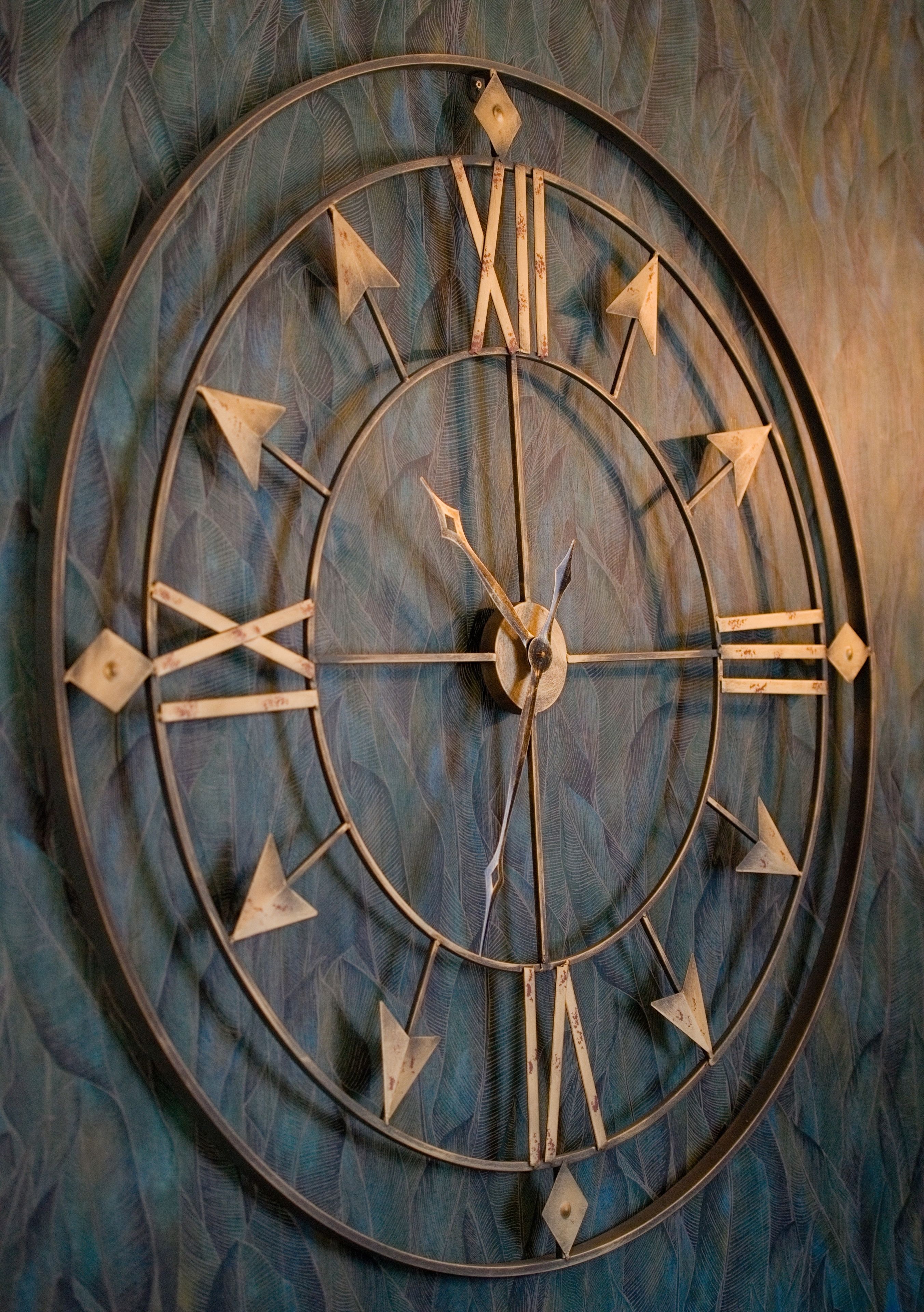 Un reloj de pared circular con números romanos y agujas de flecha, sobre un muro con textura.