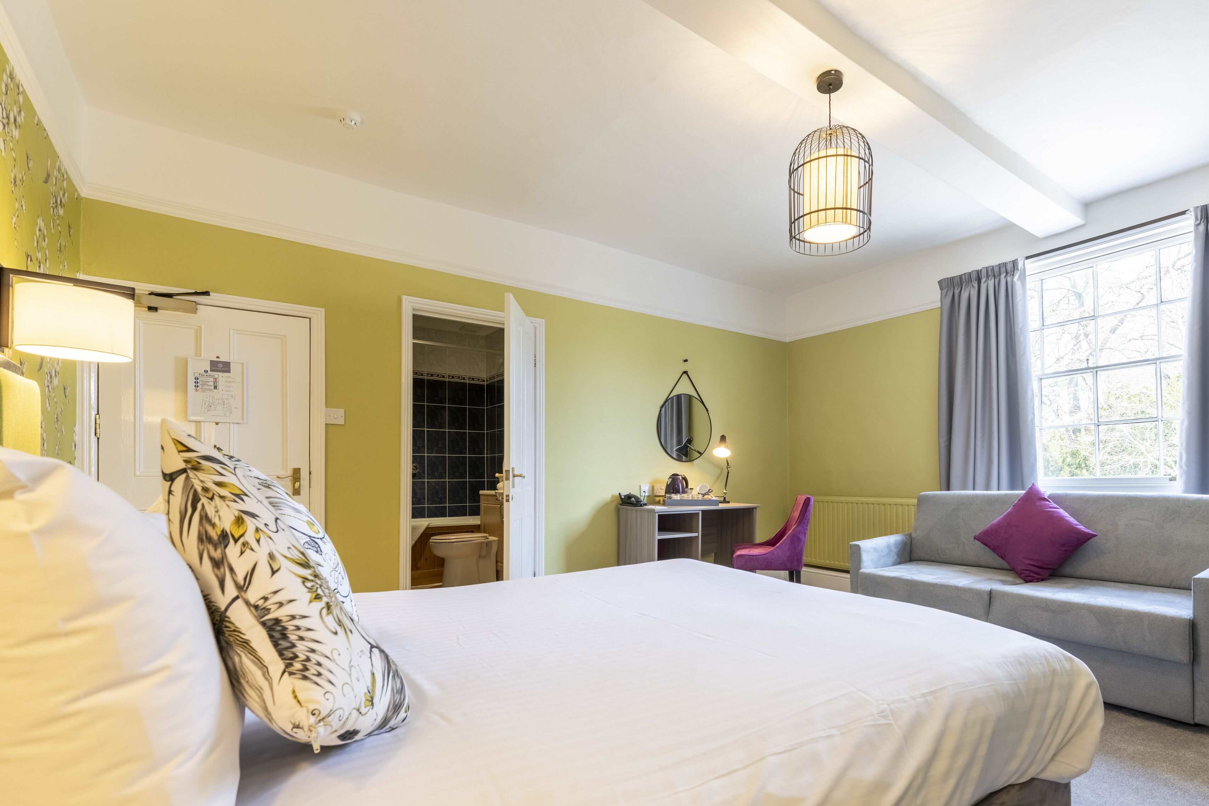 A bedroom with a bed, a desk, a chair, a sofa, and a window with curtains.