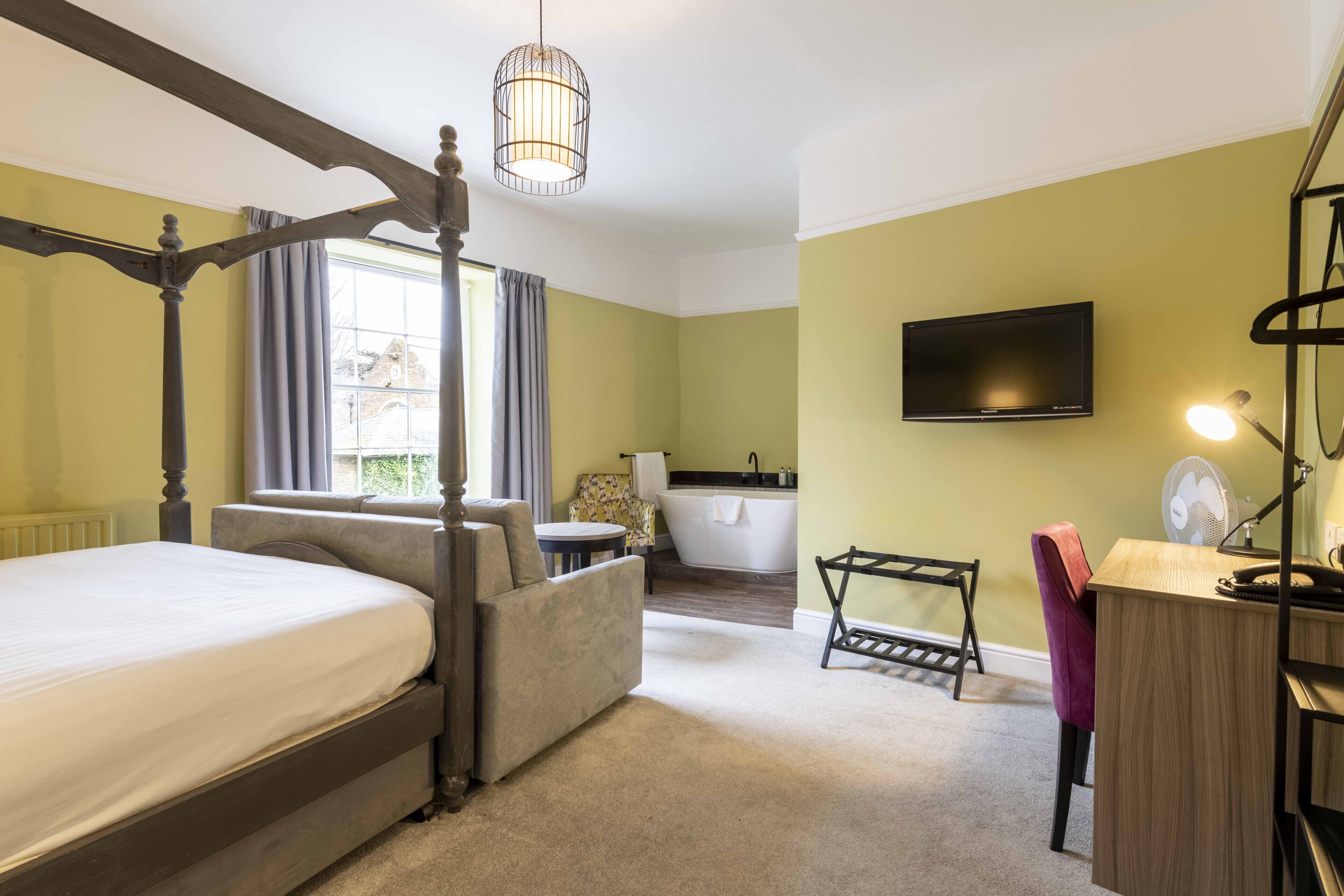 Ein Schlafzimmer mit Himmelbett, Schreibtisch mit Stuhl, Badewanne und einem Fernseher an der Wand.