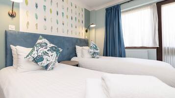 A hotel room with two beds, a headboard, wall art, a lamp, and a window with curtains.