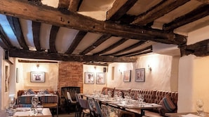 A cozy restaurant with wooden beams, leather booths, and a brick wall. Tables are set with wine glasses and plates. - The Wisteria Hotel (Oakham)