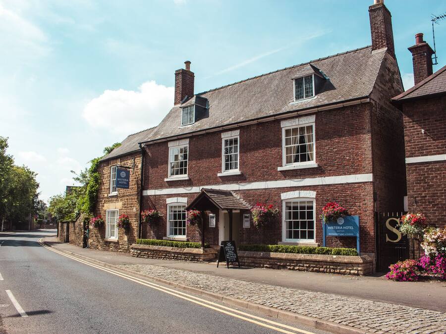 Un bâtiment traditionnel en briques, avec une enseigne indiquant «
Hôtel Wisteria
» et un petit porche orné de fleurs.