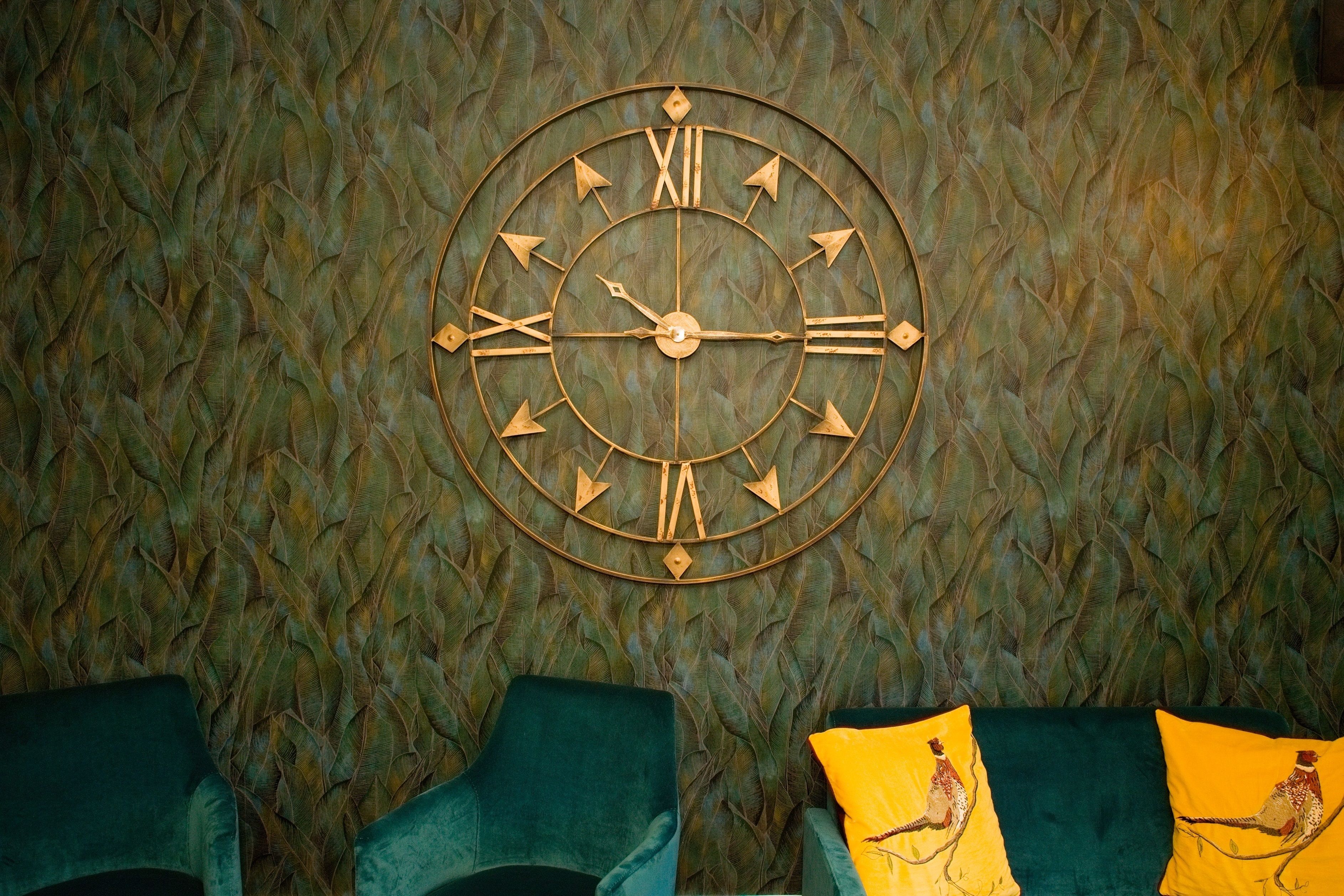Une horloge murale avec des chiffres romains et un motif décoratif représentant des plumes.