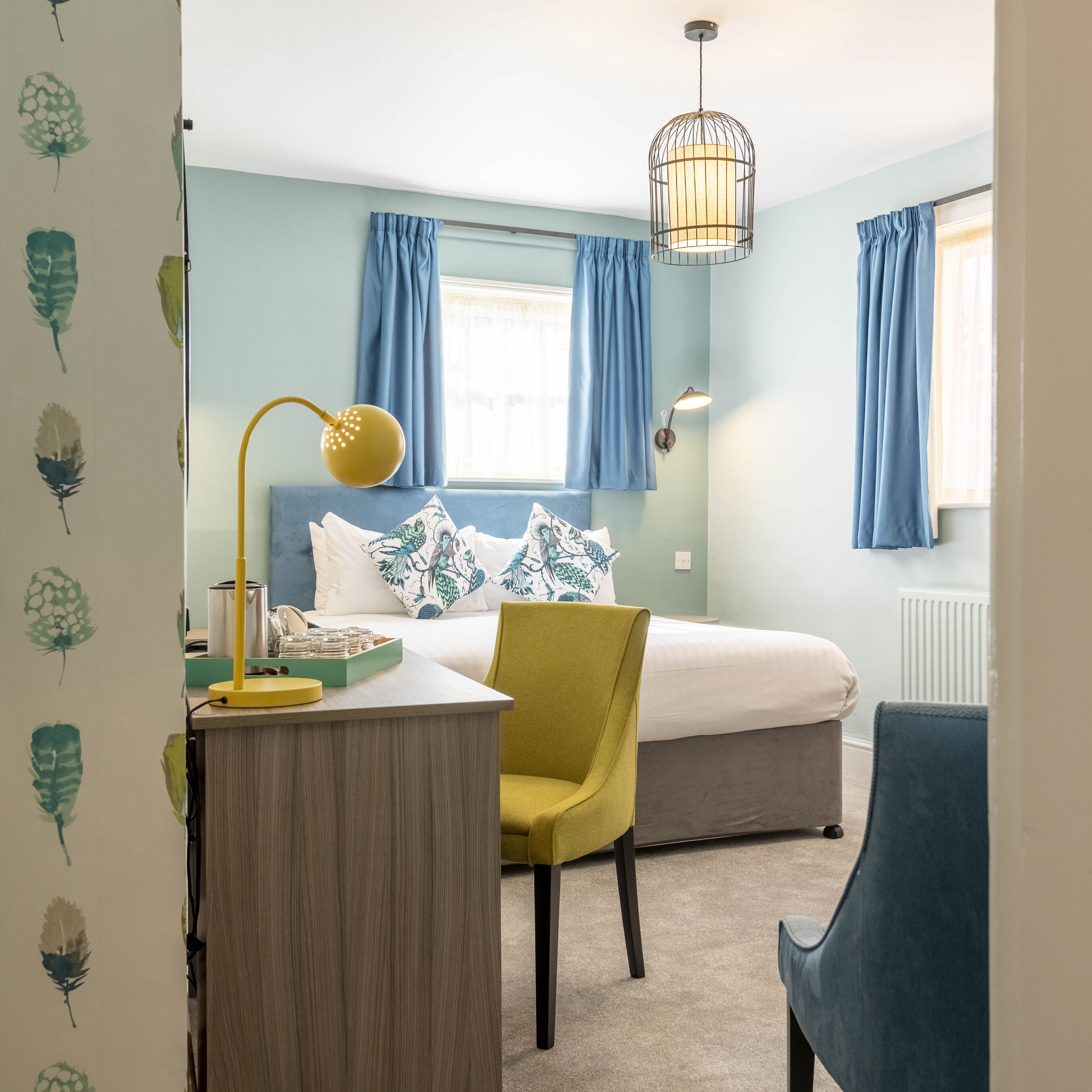 A bedroom with a bed, a desk, a chair, a lamp, and a window with curtains.