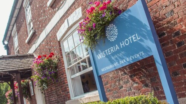 A brick building with a sign for Wisteria Hotel, indicating it offers a restaurant, bar, and events. - The Wisteria Hotel (Oakham)