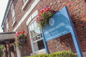 A brick building with a sign for Wisteria Hotel, indicating it offers a restaurant, bar, and events. - The Wisteria Hotel (Oakham)