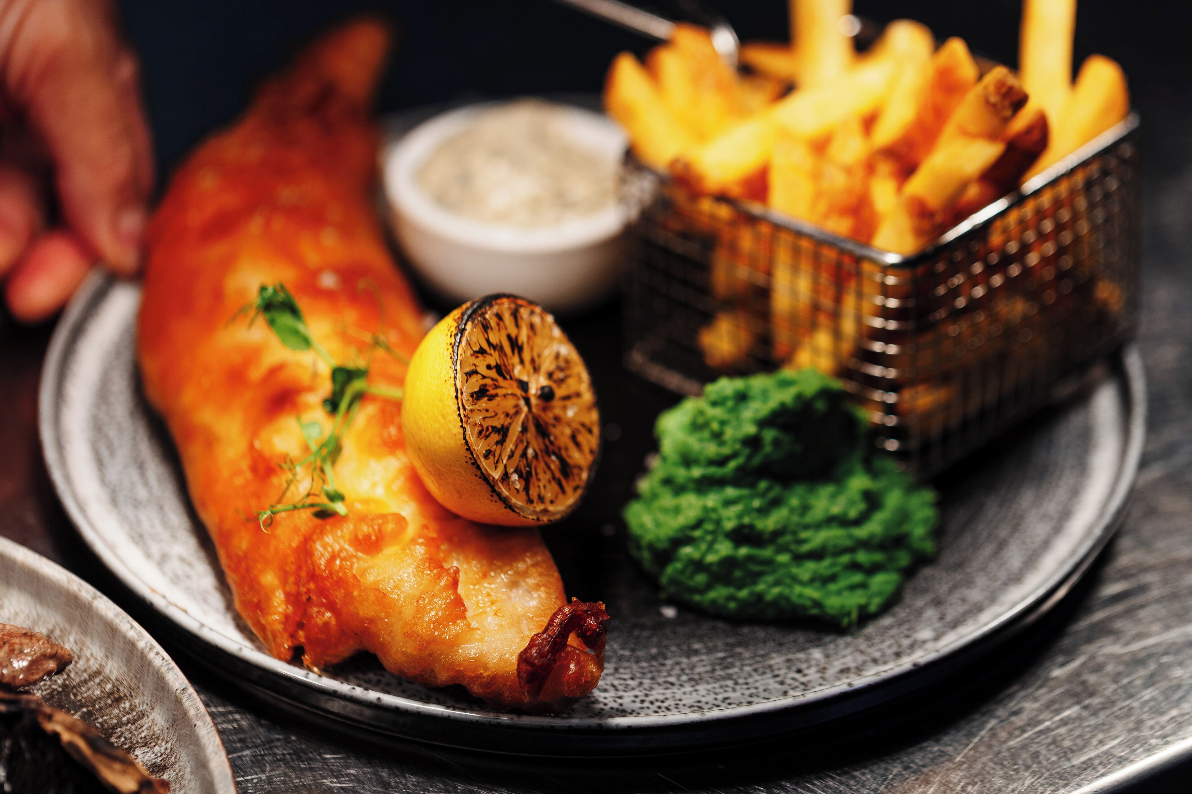 A plate with fish, chips, and a small bowl of sauce.
