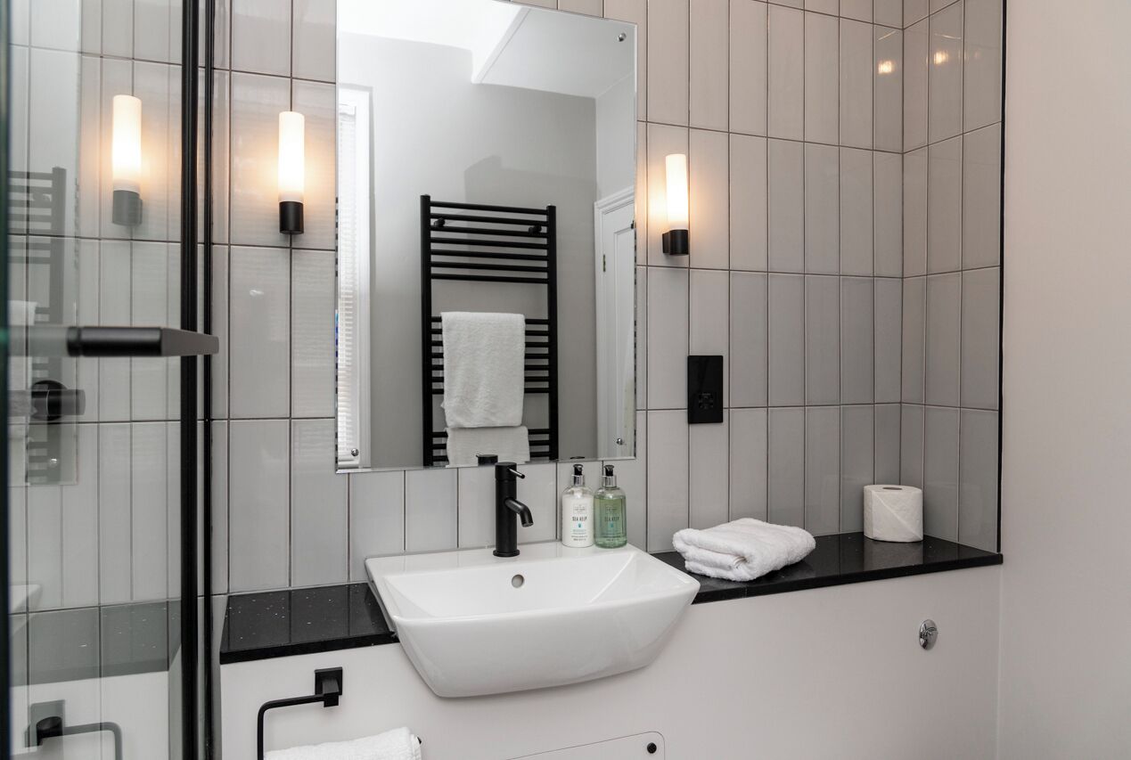 A modern bathroom with a white sink, black faucet, and a glass shower enclosure.