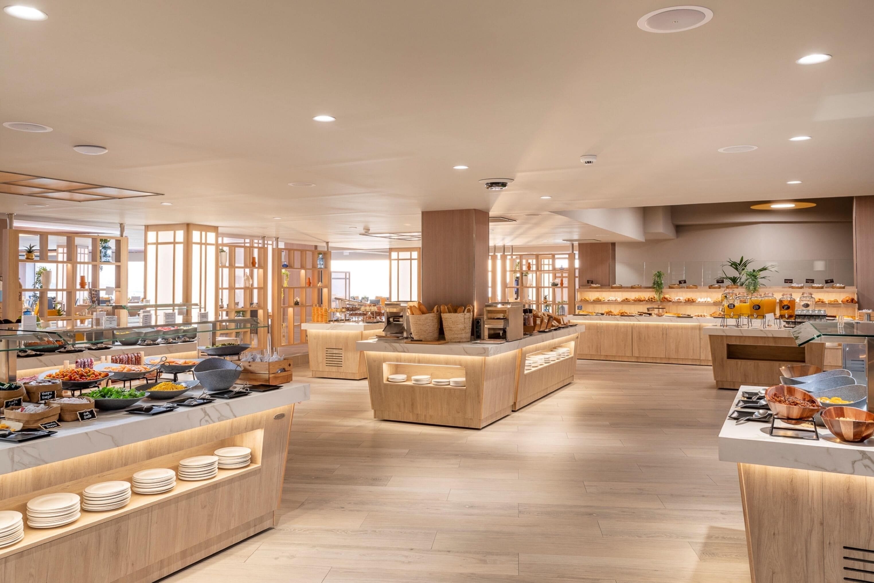 Un área de desayuno moderna con mostradores de madera, diversos alimentos y un interior limpio y bien iluminado.