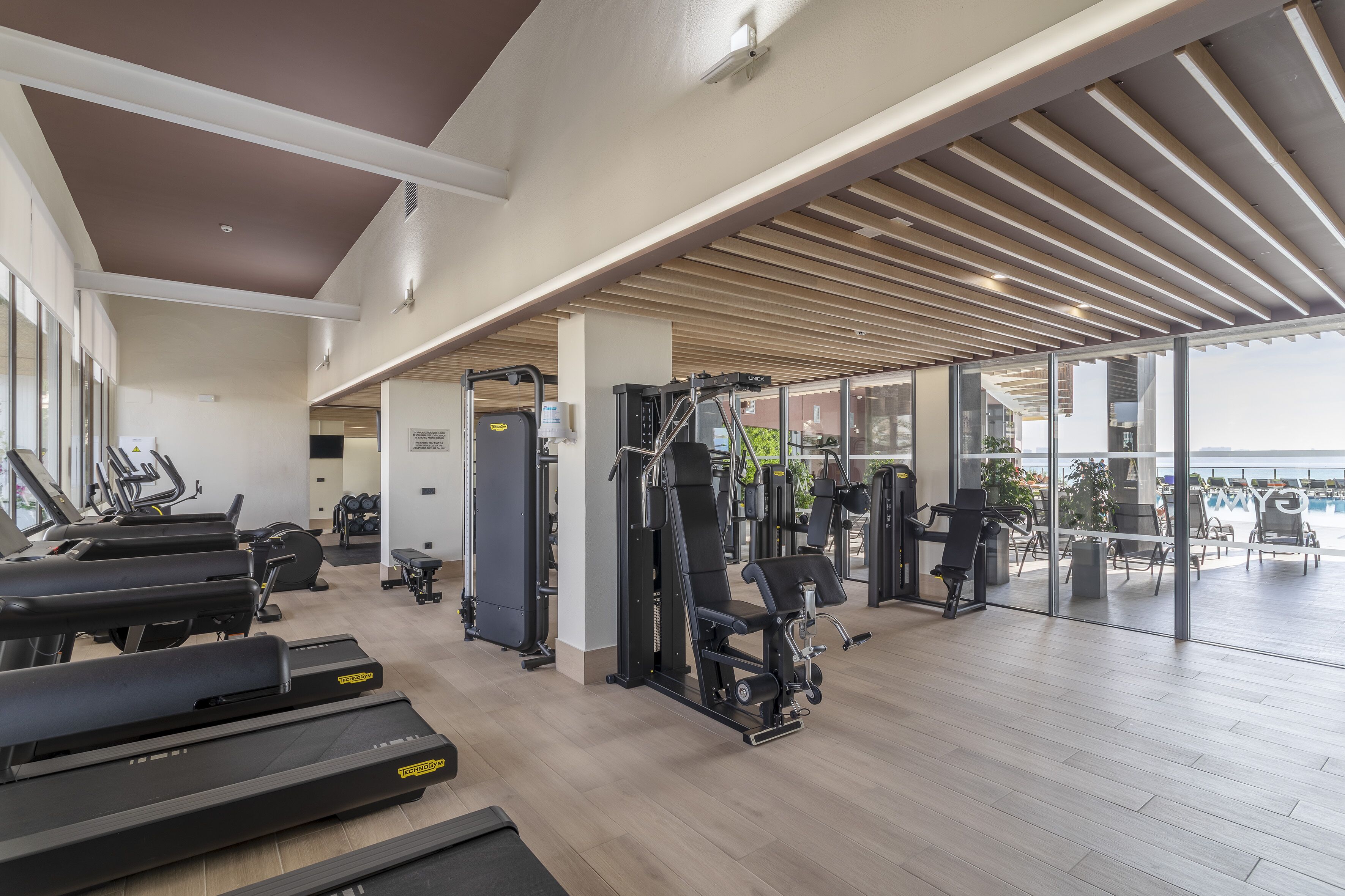 Un gimnasio moderno con cintas de correr, máquinas de pesas y un amplio ventanal con vistas al exterior.