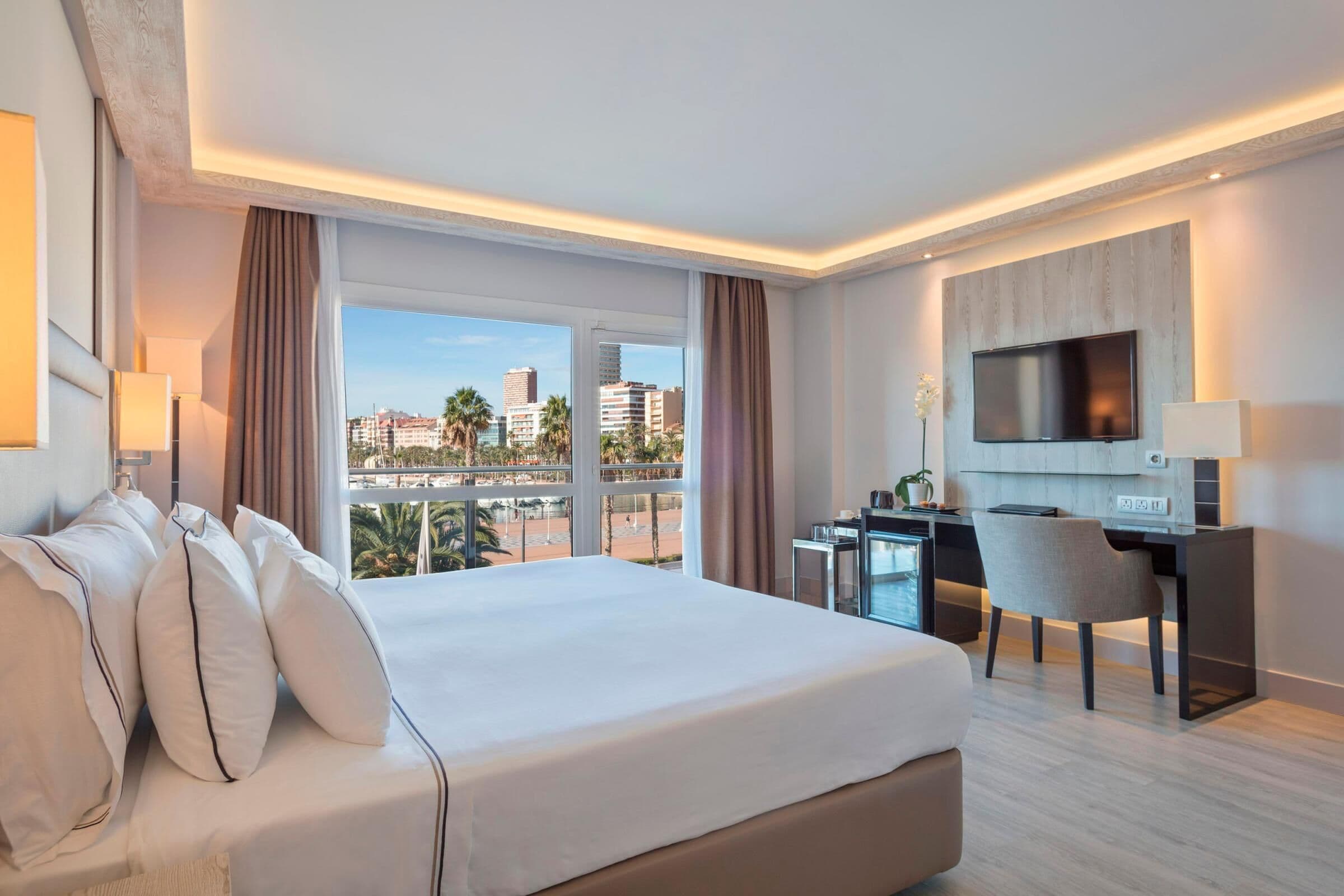 Een hotelkamer met een groot bed, een bureau, een stoel, een televisie en uitzicht op de stad.
