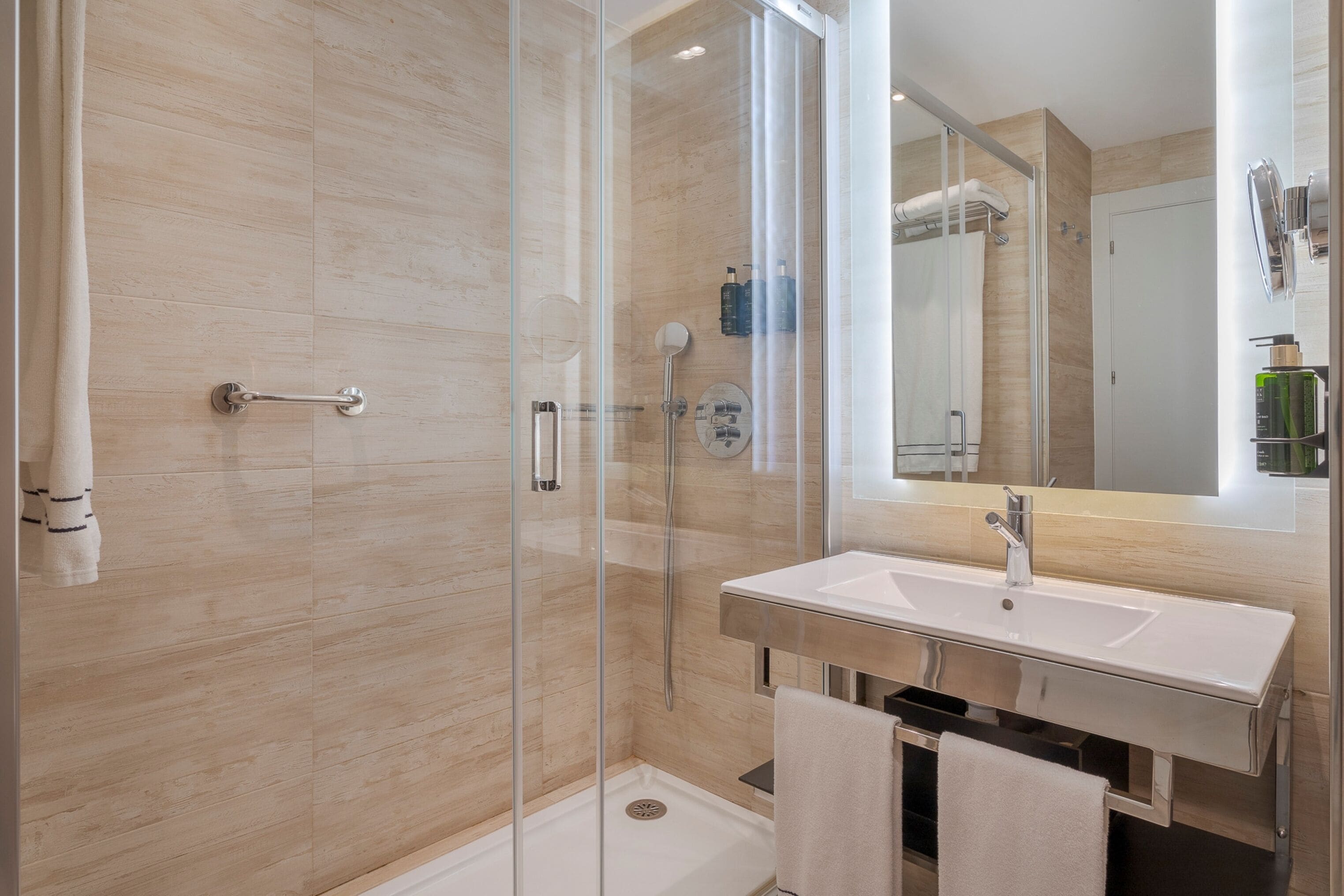 Un baño moderno con ducha envuelta en vidrio, un lavabo blanco y un espejo grande.