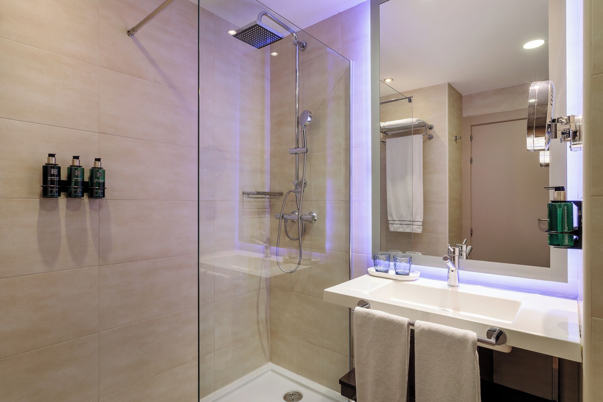 A modern bathroom with a glass-enclosed shower, a white sink, and a large mirror.