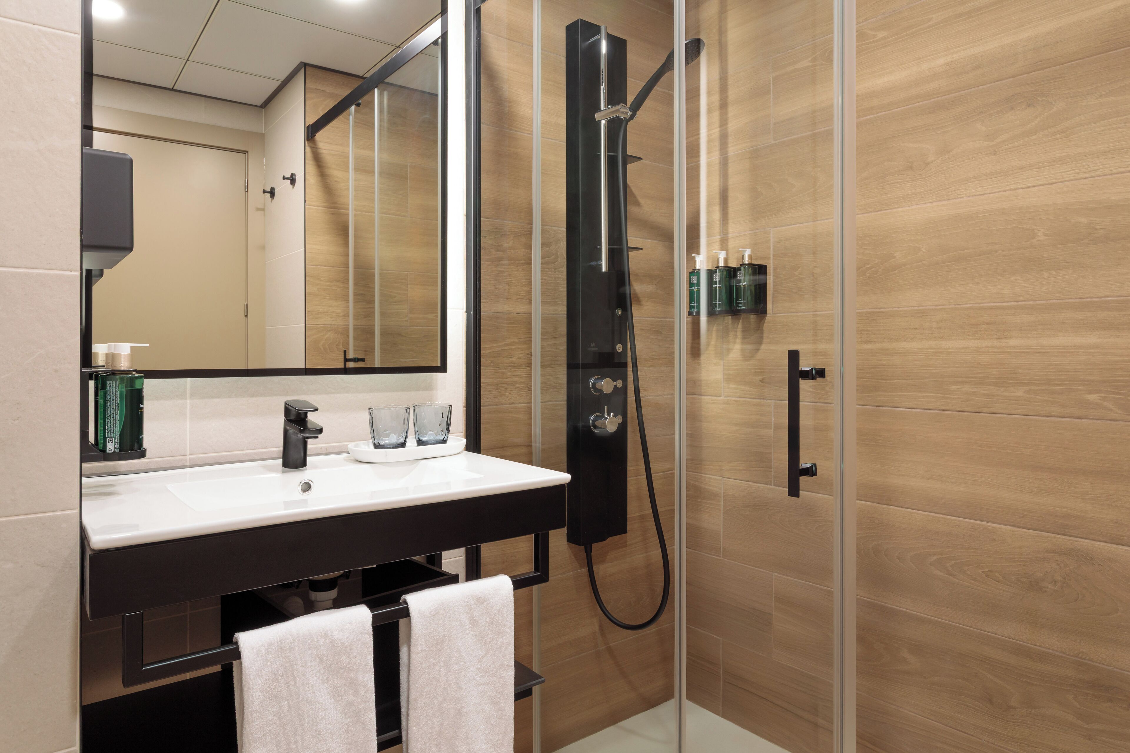 Un baño moderno con ducha de vidrio, un lavamanos negro y un espejo encima.