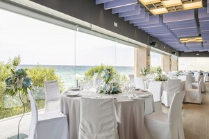 Un salón de banquetes con mesas redondas dispuestas para un evento formal, con vistas a una masa de agua.