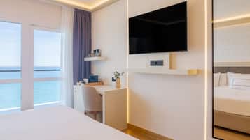 Habitación de hotel moderna con una cama grande, un escritorio con una silla, un televisor montado en la pared y vistas al mar a través de la ventana.