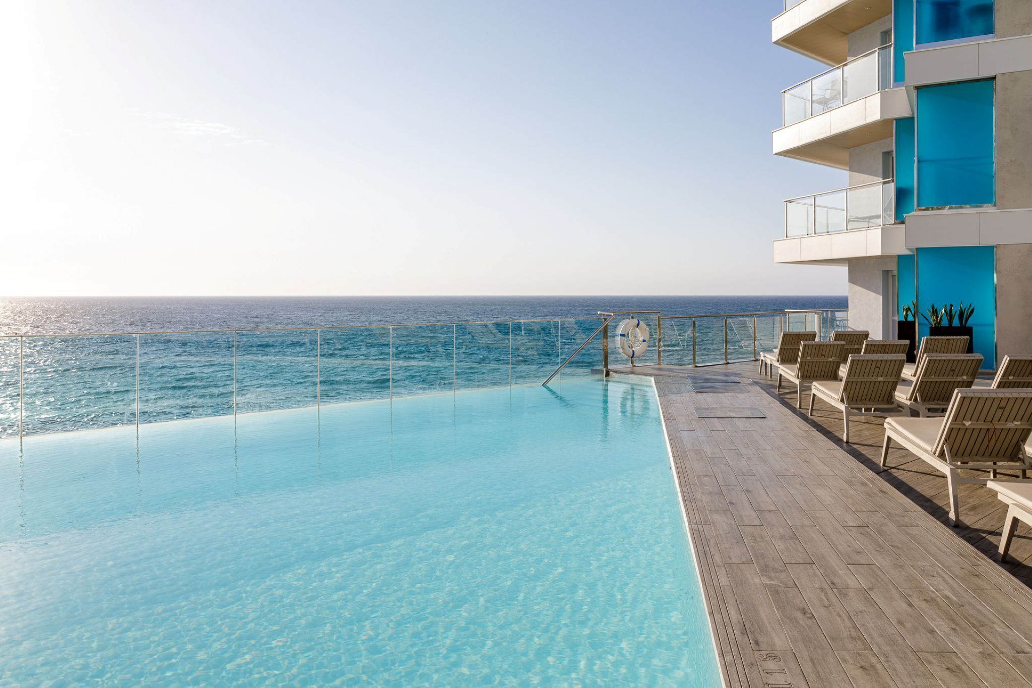 A poolside area with a view of the ocean, lounge chairs, and a lifebuoy.