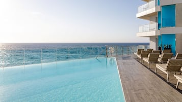Zona junto a la piscina con vista al océano, sillas de descanso y un flotador.