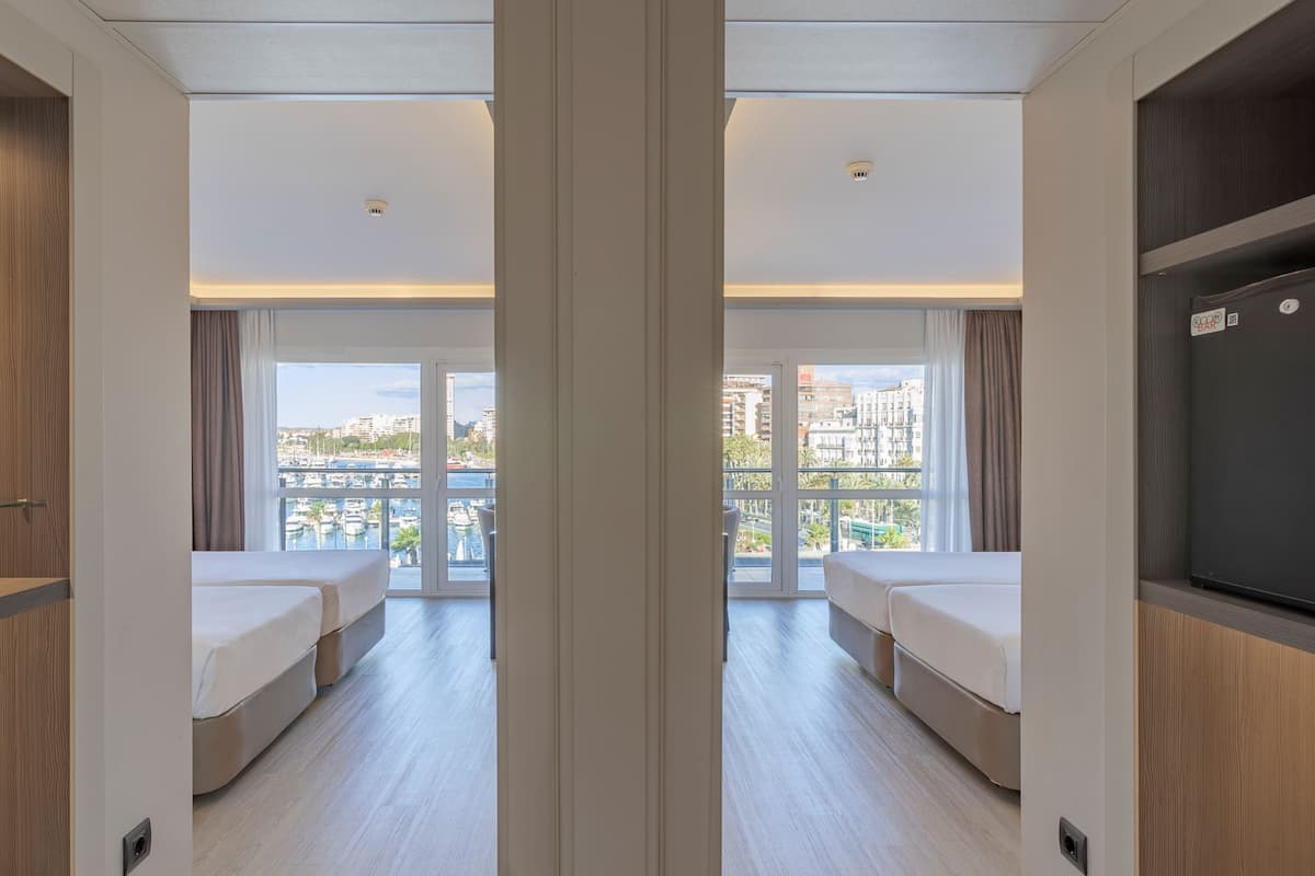 Habitación de hotel con dos camas, televisión y ventana grande con vista a la ciudad.