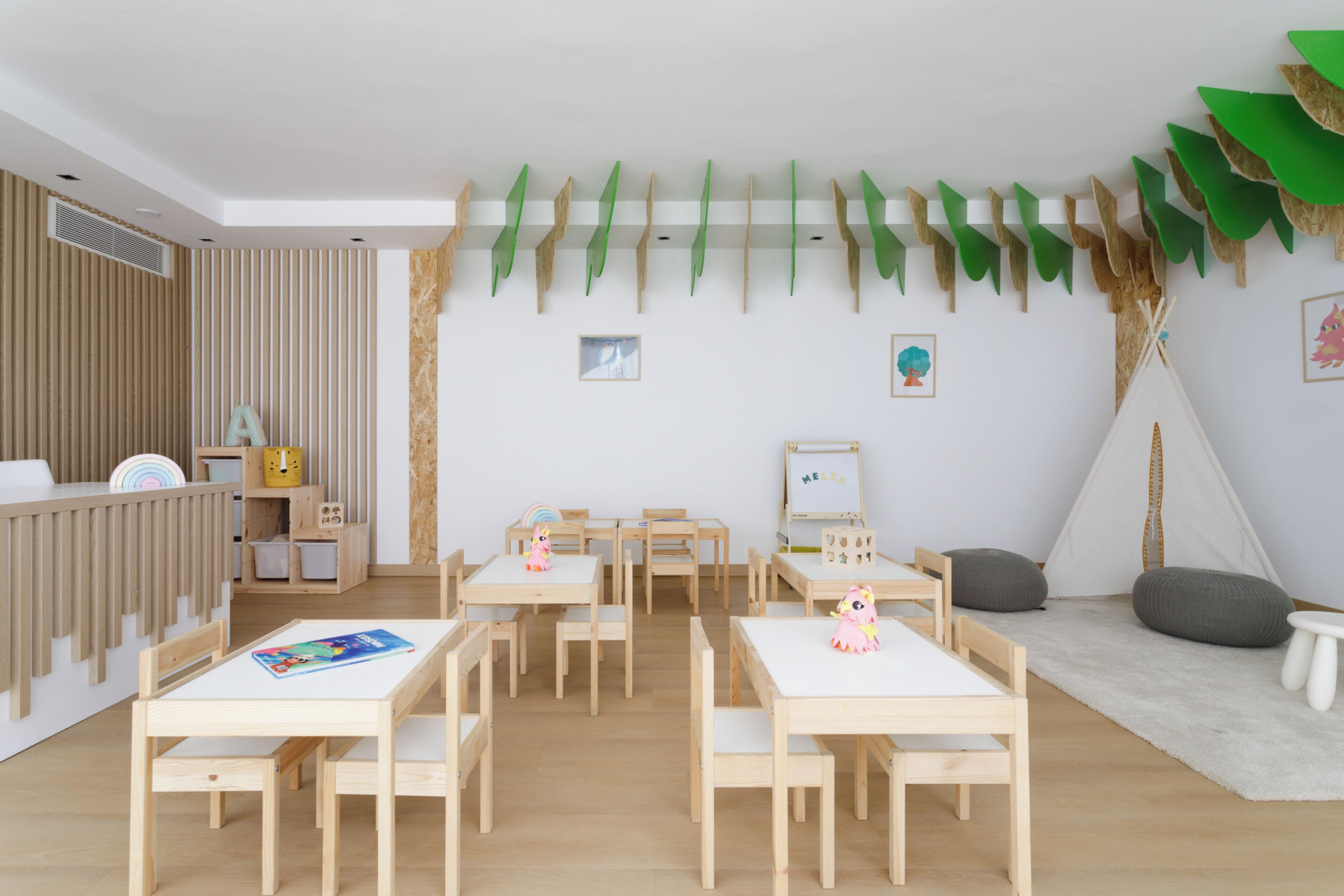 Ein Spielzimmer für Kinder mit Holzmöbeln, einer Whiteboard-Tafel und einer Zeltdach-Konstruktion.